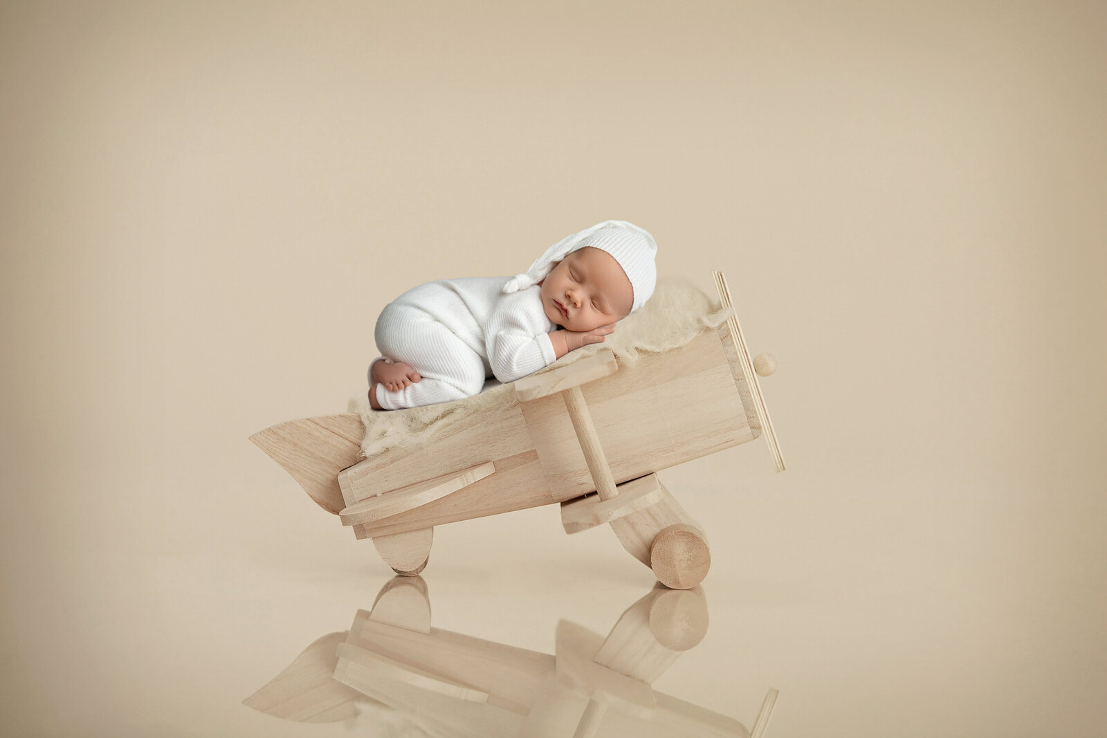Baby boy in a white romper, sleeping on wooden airplane. Photographed by Jenni Nikki at Atlanta photo studio.