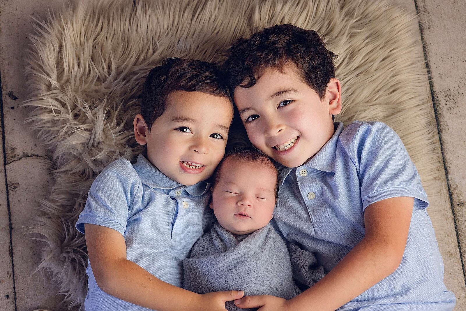 A photo of two boys holding their newborn brother, taken by Bia Schaefer during an in-home newborn session in Central Florida.
