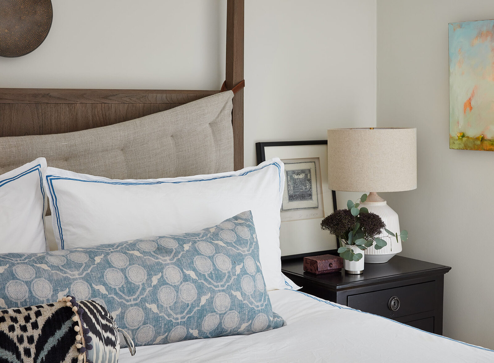 Canopy bed with white comforter and blue pillows and a dark wooden nightstand
