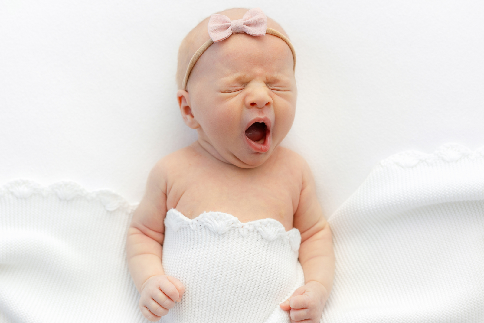 newborn wearing pink bow yawns during boston newborn photography session