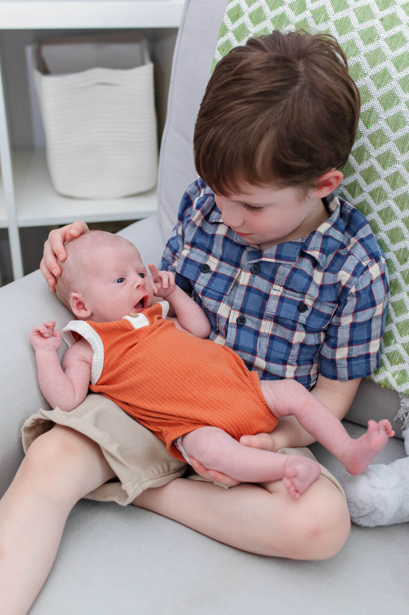 A newborn boy being held in a chair by his big brother.
