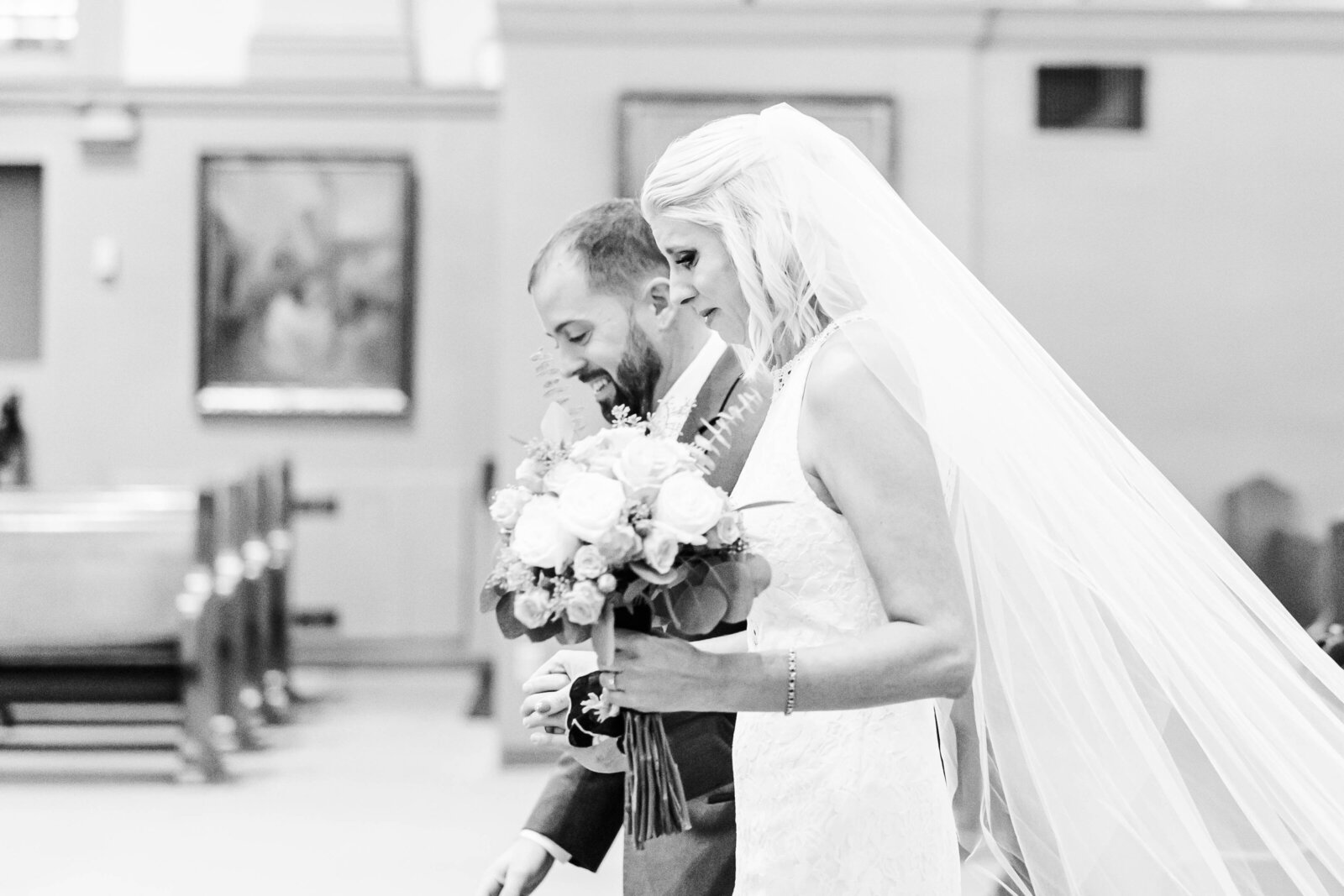 Bride and groom hold hands while bride is holding her bouquet as they walk up the steps in the church during their wedding ceremony by Kansas City Wedding Photographer Sarah Riner Photography