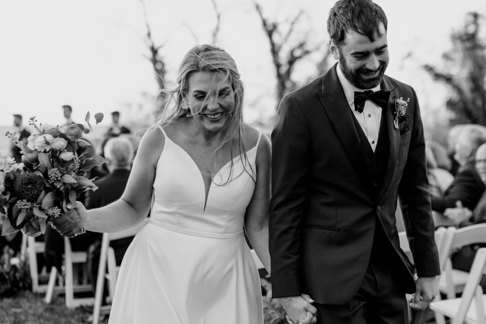 A bride and groom hold hands and smile while walking up the aisle