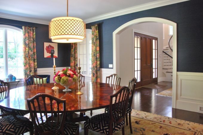 A navy formal dining room with a round wooden table and eight chairs.