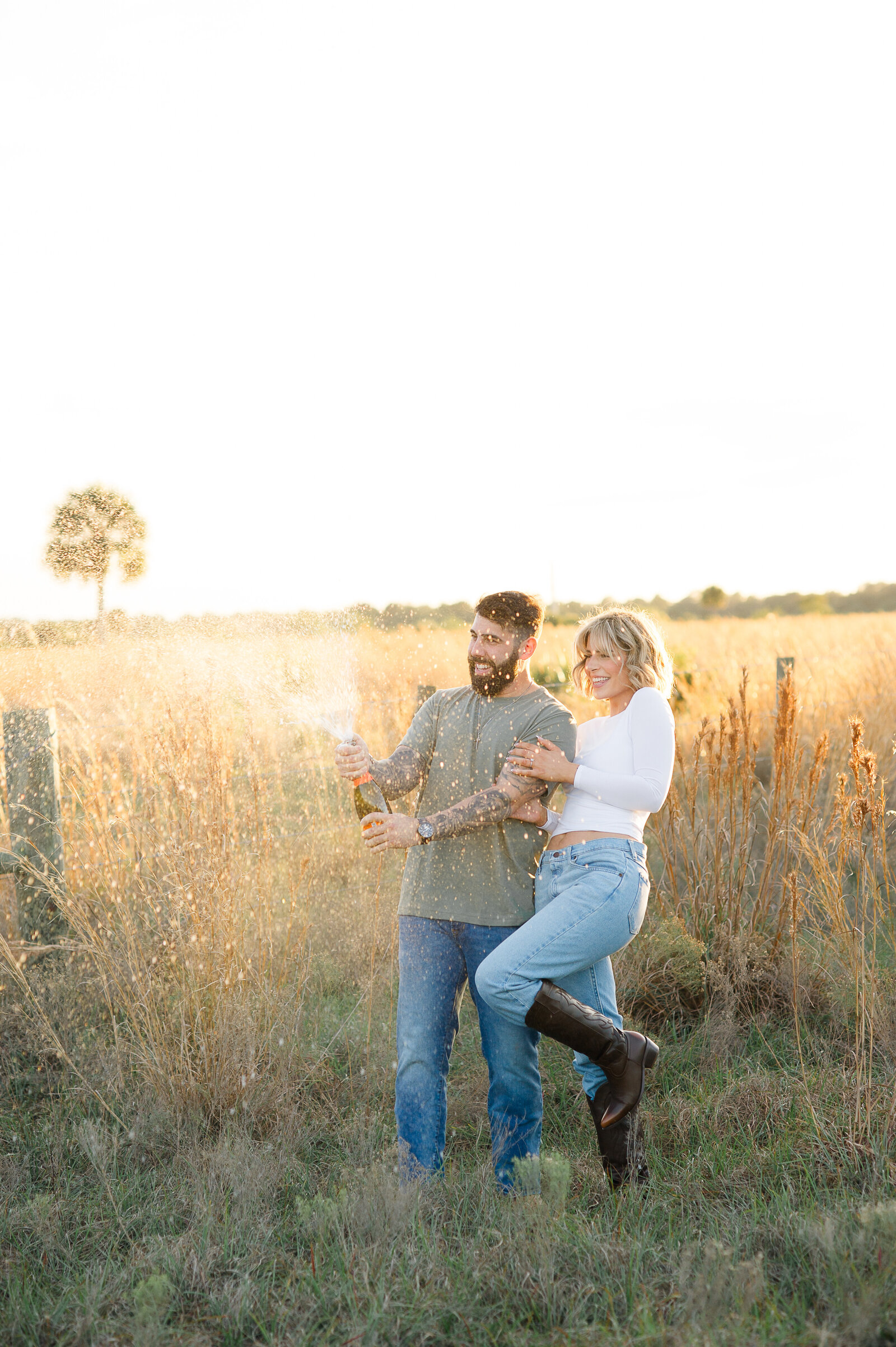 Newly engaged couple pops a bottle of champagne in a field during their engagement photo session