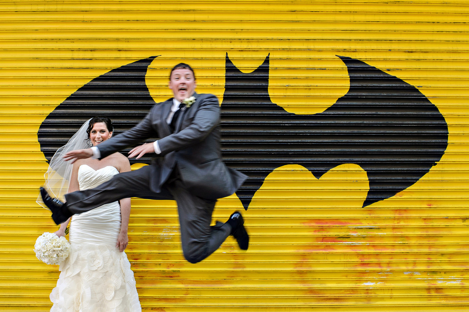 A wedding couple jump for love in front of batman graffiti on South Street in Philadelphia.