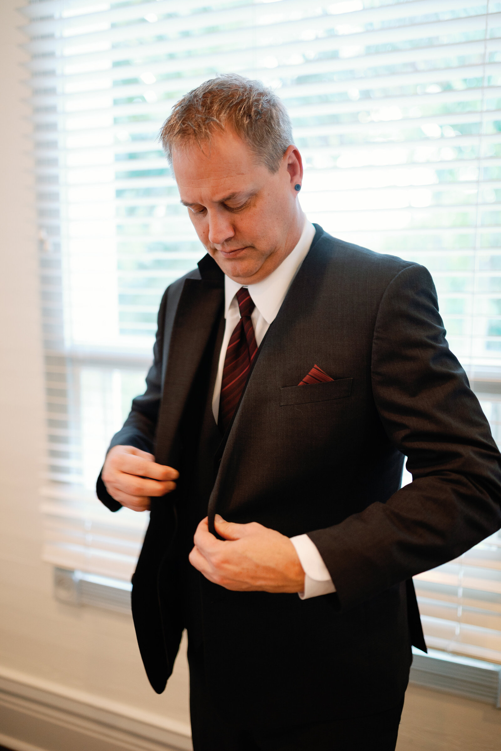 Groom about to button up his wedding day suit jacket