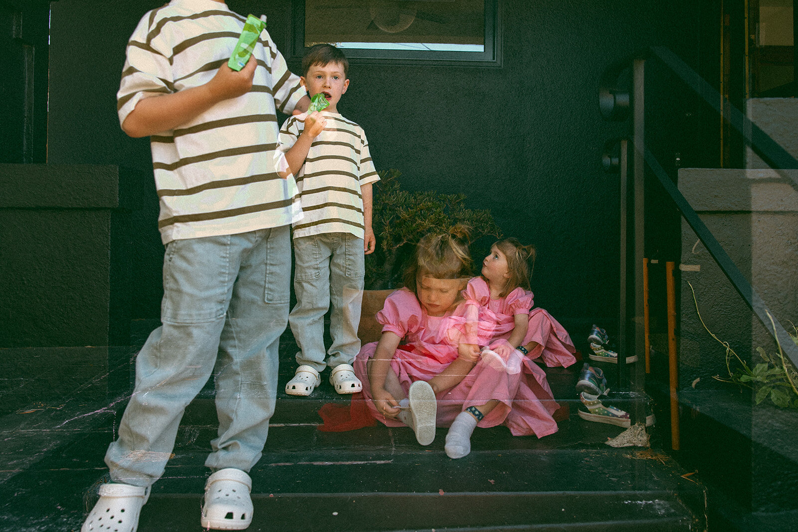 double exposure of young boy standing eating an applesauce pouch while sister in princess dress puts on her shoes