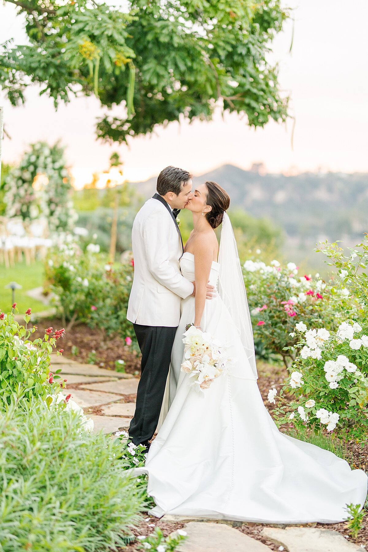 Bride and groom kissing among white flowers in the garden at a private residence in Rancho Santa Fe, California.