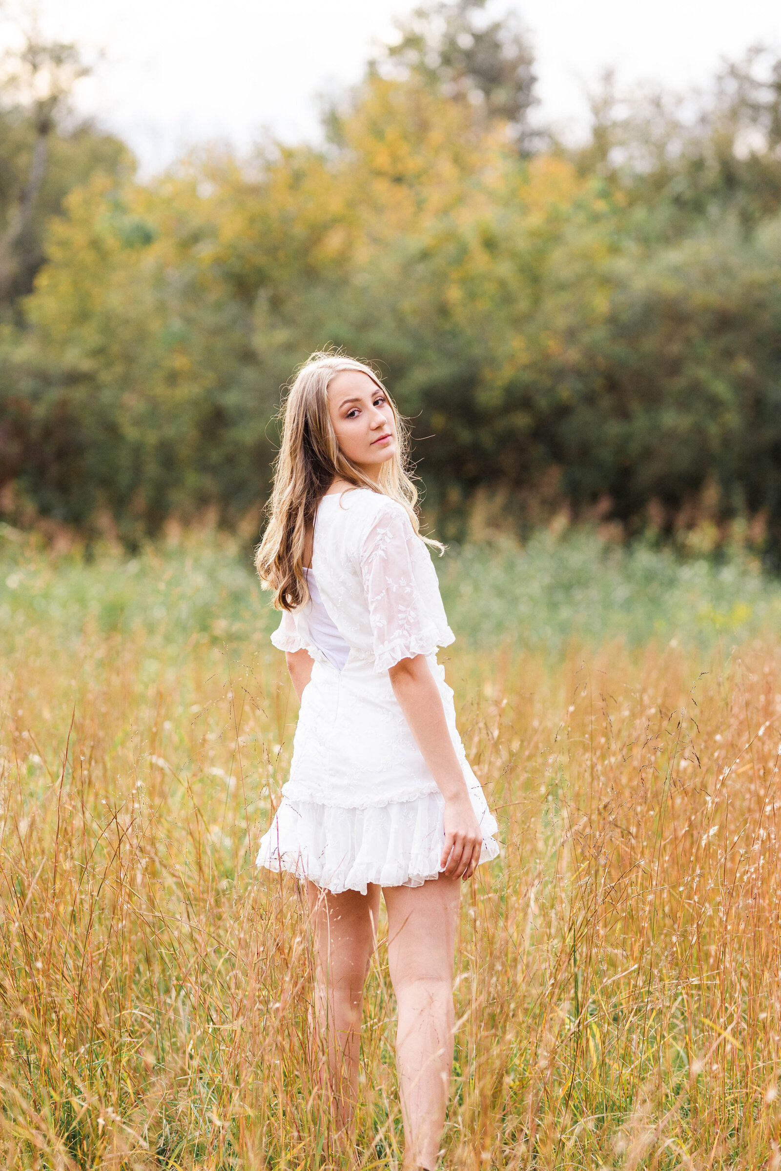 high school senior wearing a white dress walking in a field