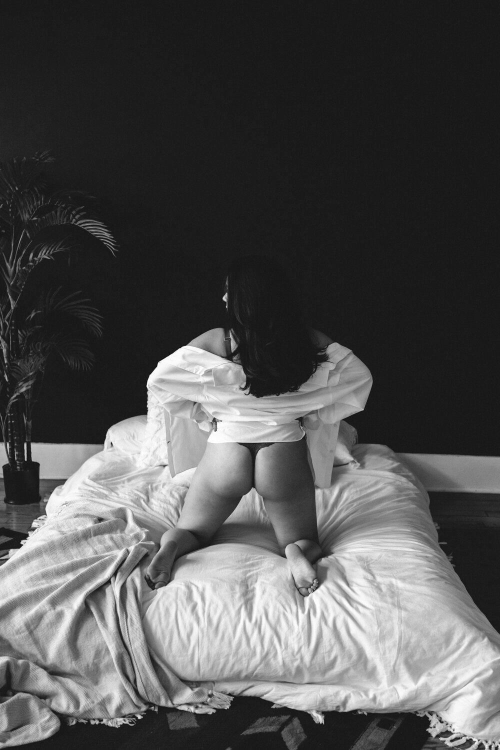 Black and white photo of a girl with black hair wearing a white button down draped over her arms captured by boudoir by Steph