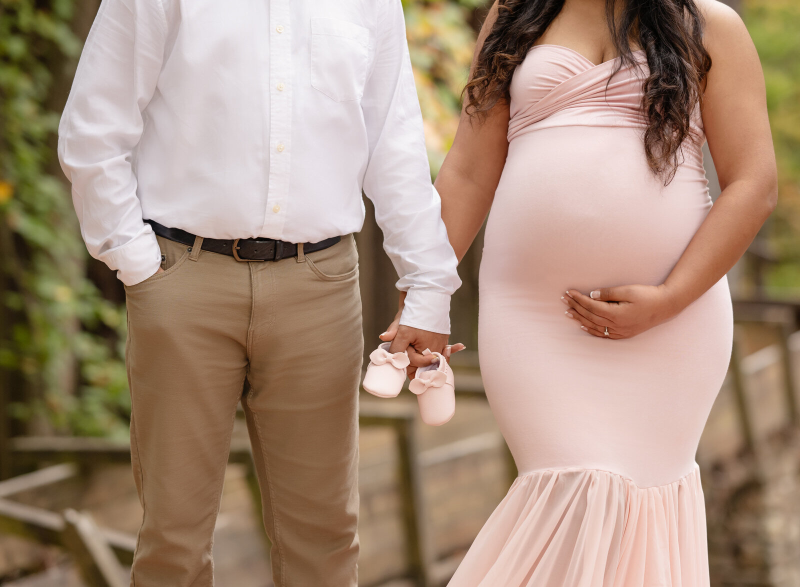 Mom and Dad holding hands with pink baby shoes for Maternity photoshoot.