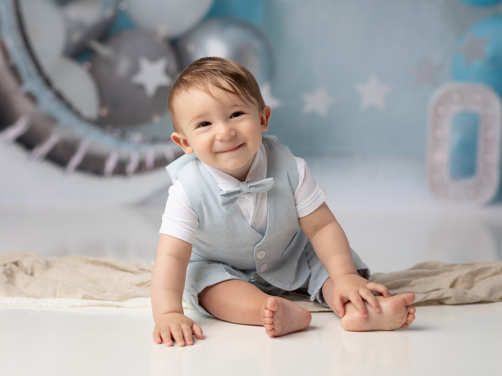 one year old boy in blue suit smiling for cake smash photoshoot