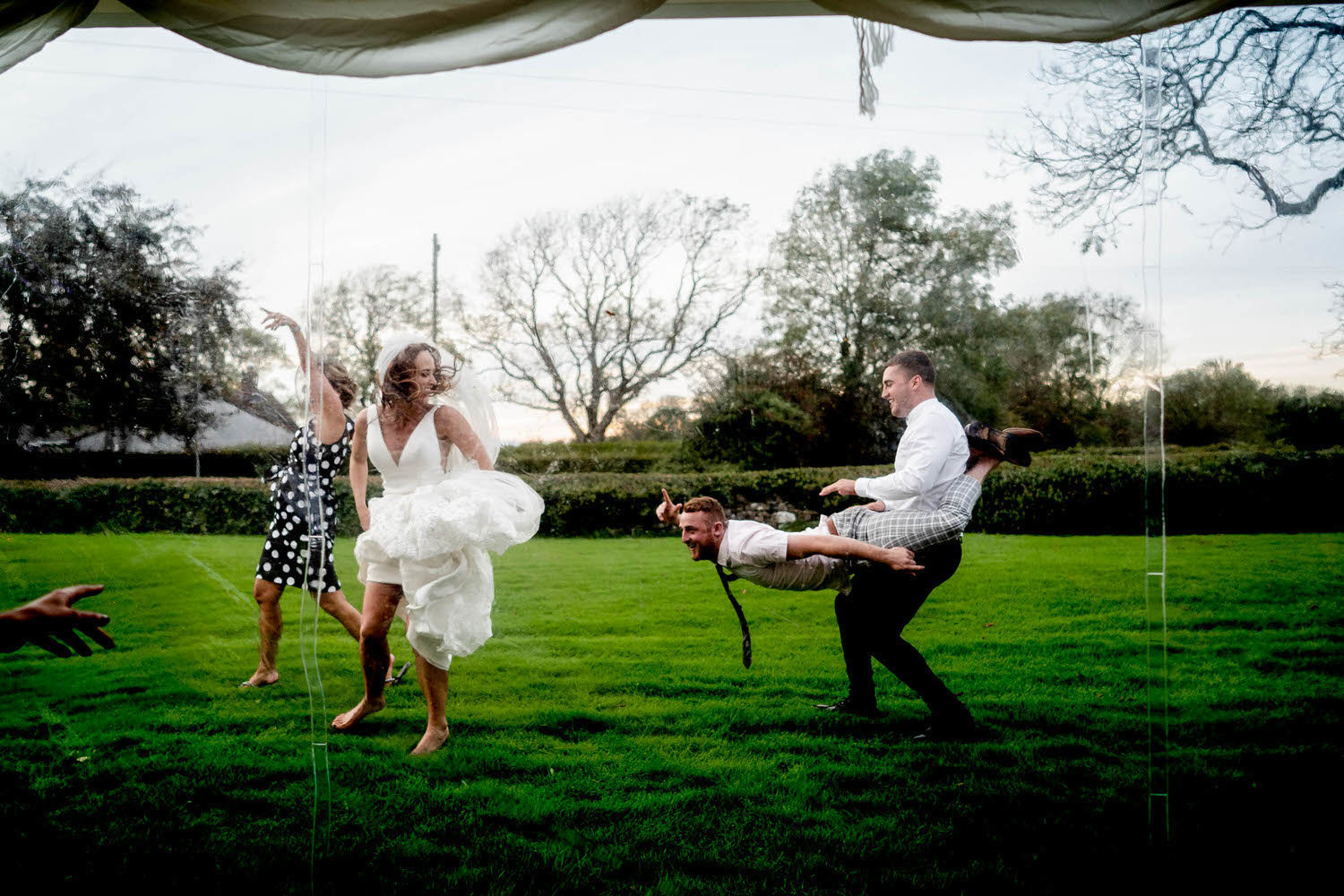 wedding party guests man wheelbarrow carrying groomsman and bride laughing