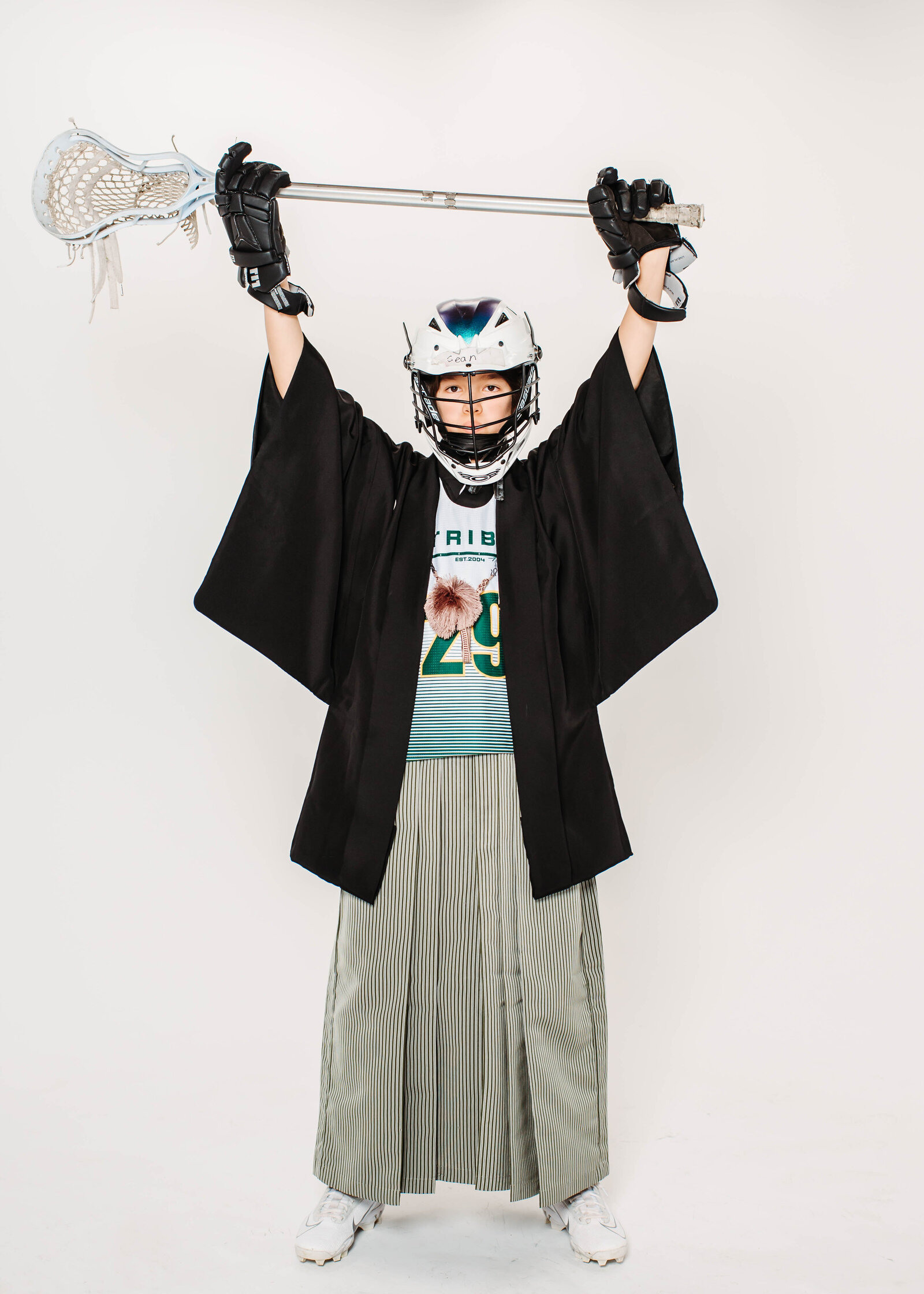 Boy wearing lacrosse uniform combined with traditional hakama, holding stick overhead for graduation photo | 卒業式 ラクロス ユニフォーム 袴 男の子 スポーツと伝統の融合