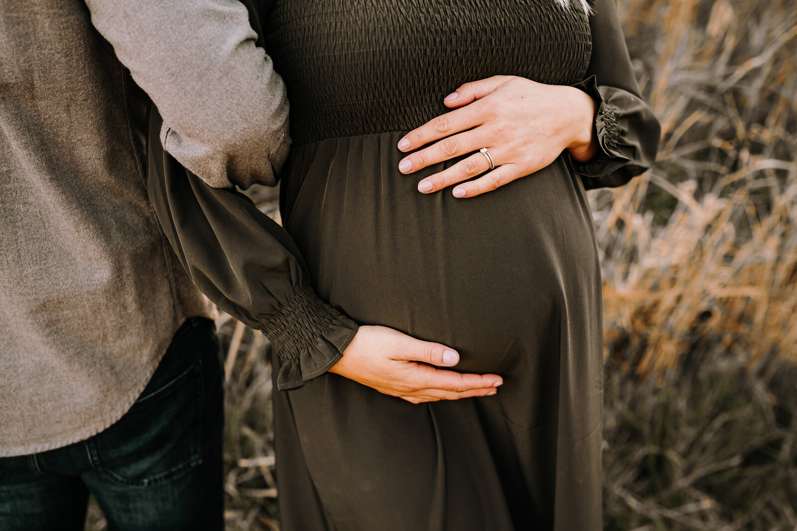 Momma to be holds on tight to a dad to be while embracing her growing baby bump during an outdoor maternity session near bismarck, ND. 