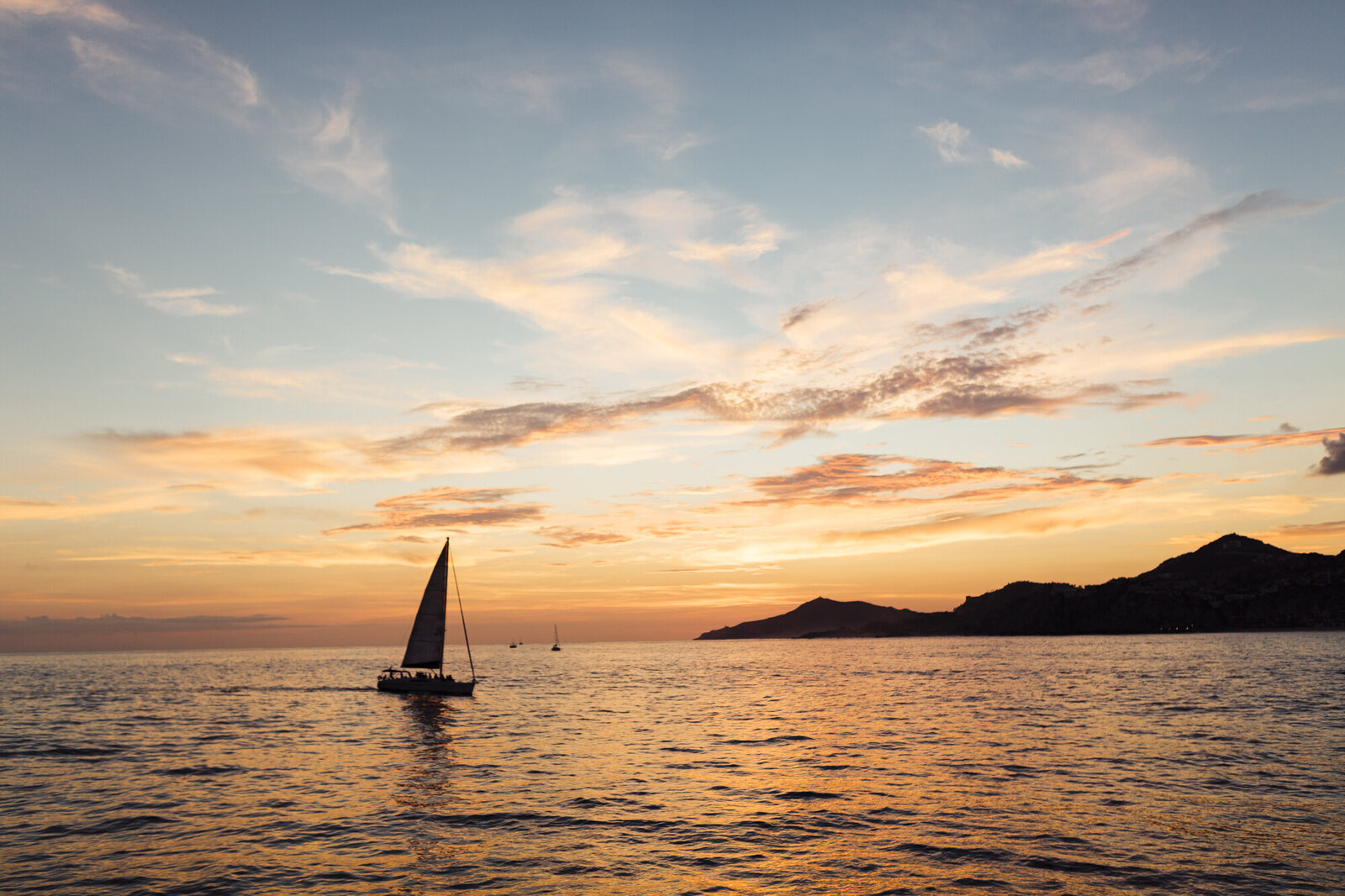 A sailboat cruising on calm waters at sunset with a colorful sky in the background, captured by a destination wedding photographer.