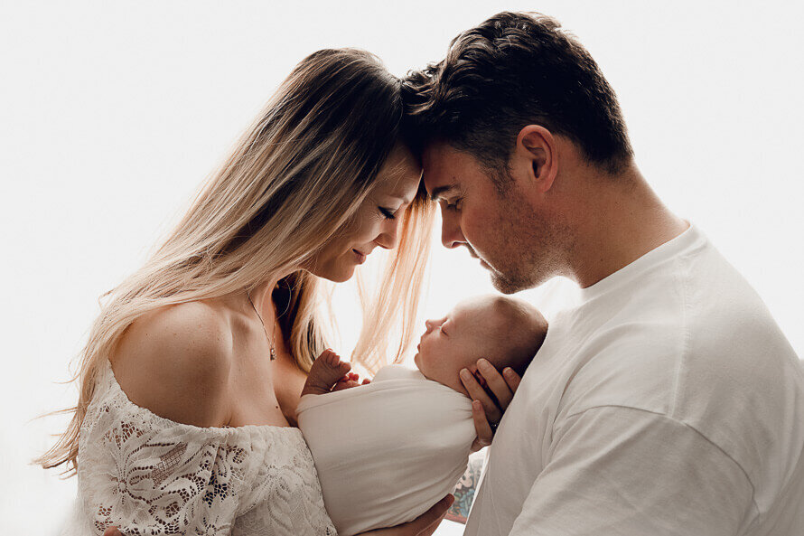 Two parents look at their newborn with their heads together.