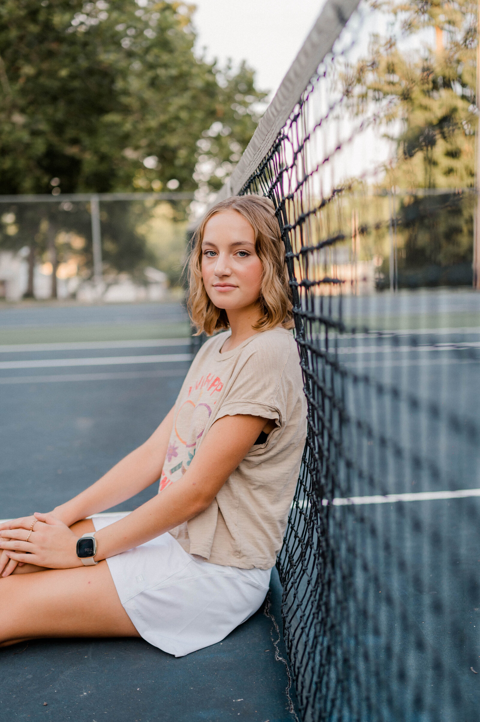 Girl poses for camera on the tennis court leaning against the net.