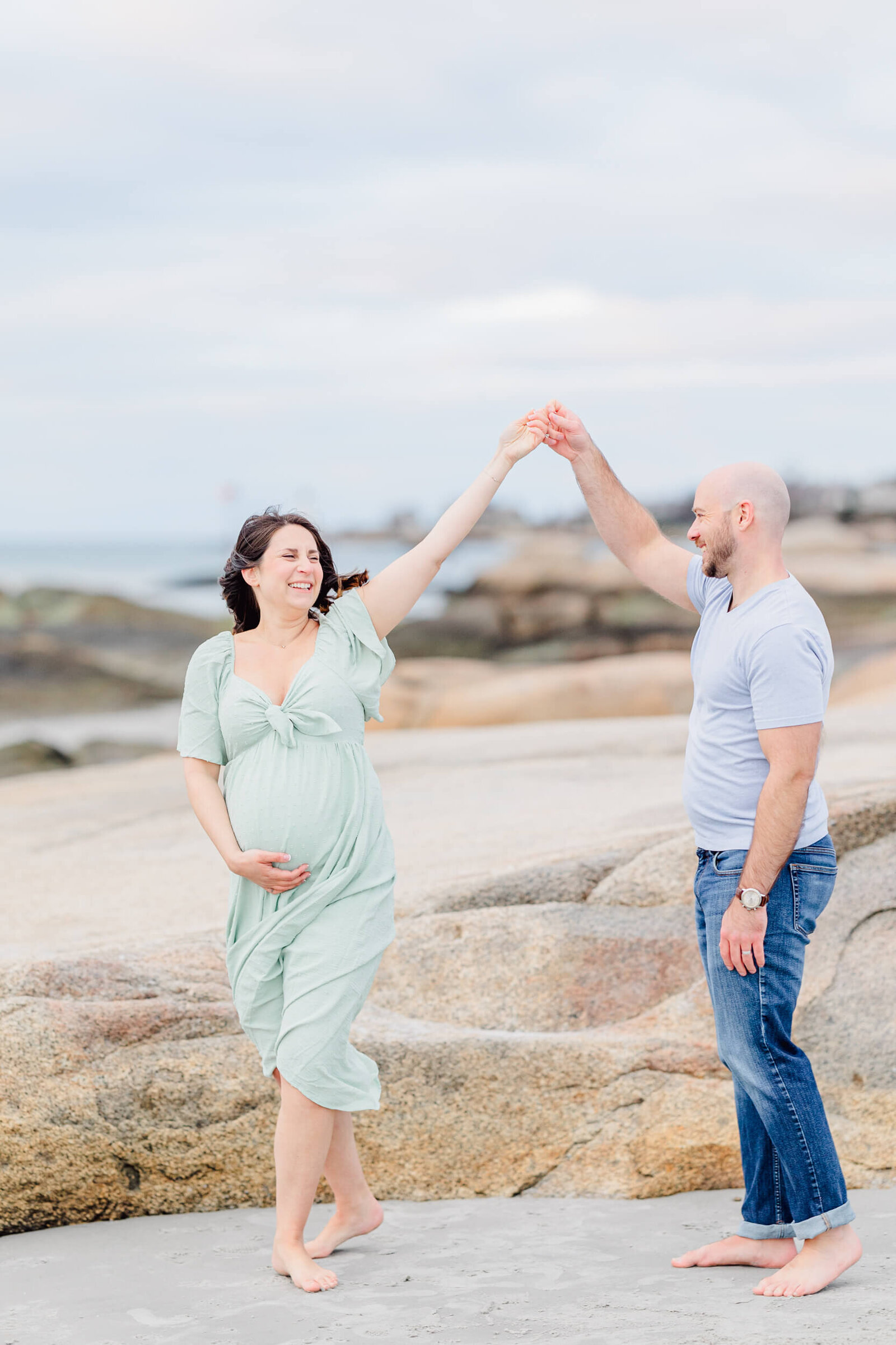 A man twirls his pregnant, laughing wife on a beach north of Boston