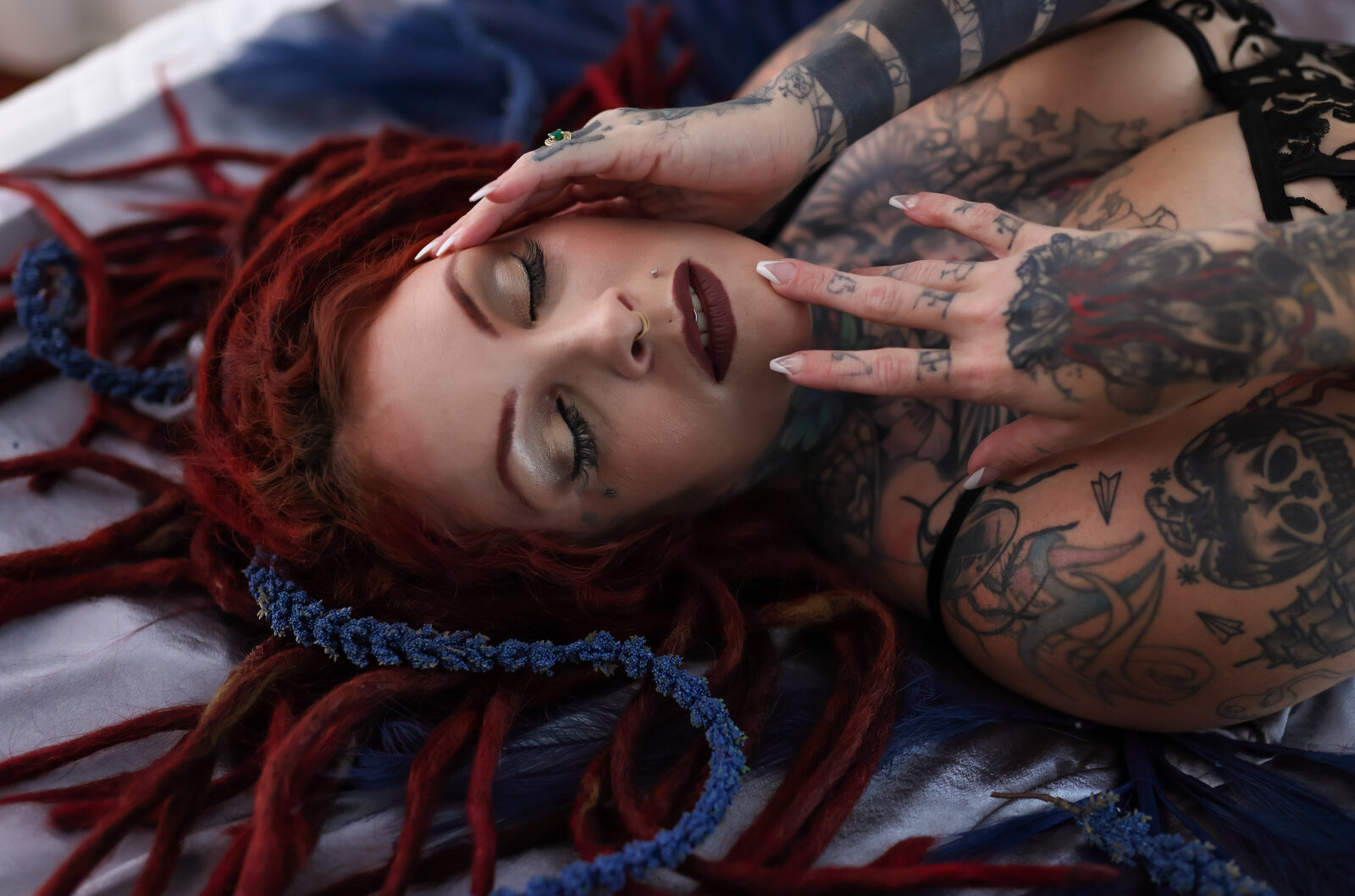 Savannah Georgia Boudoir Photography and Glamour boudoir portrait of Woman with tattoos and dreadlocks laying on bed with eyes closed and hands in face