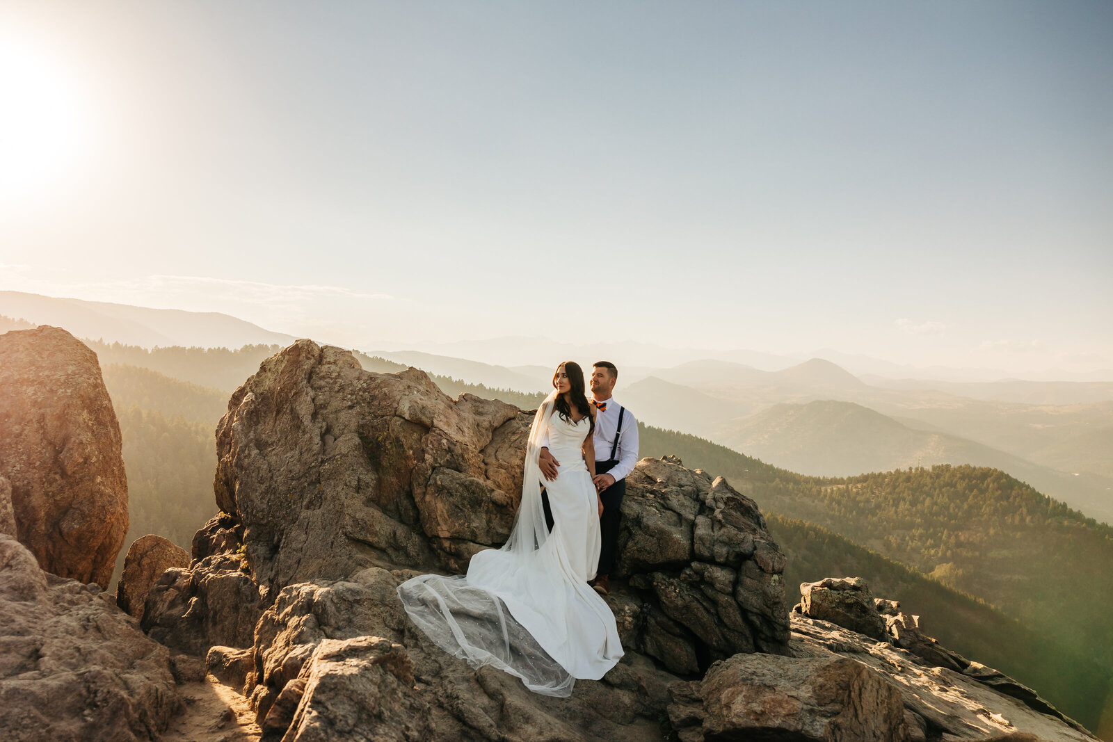 Wedding Photographer Boulder Colorado captures man holding woman by boulder after forest wedding