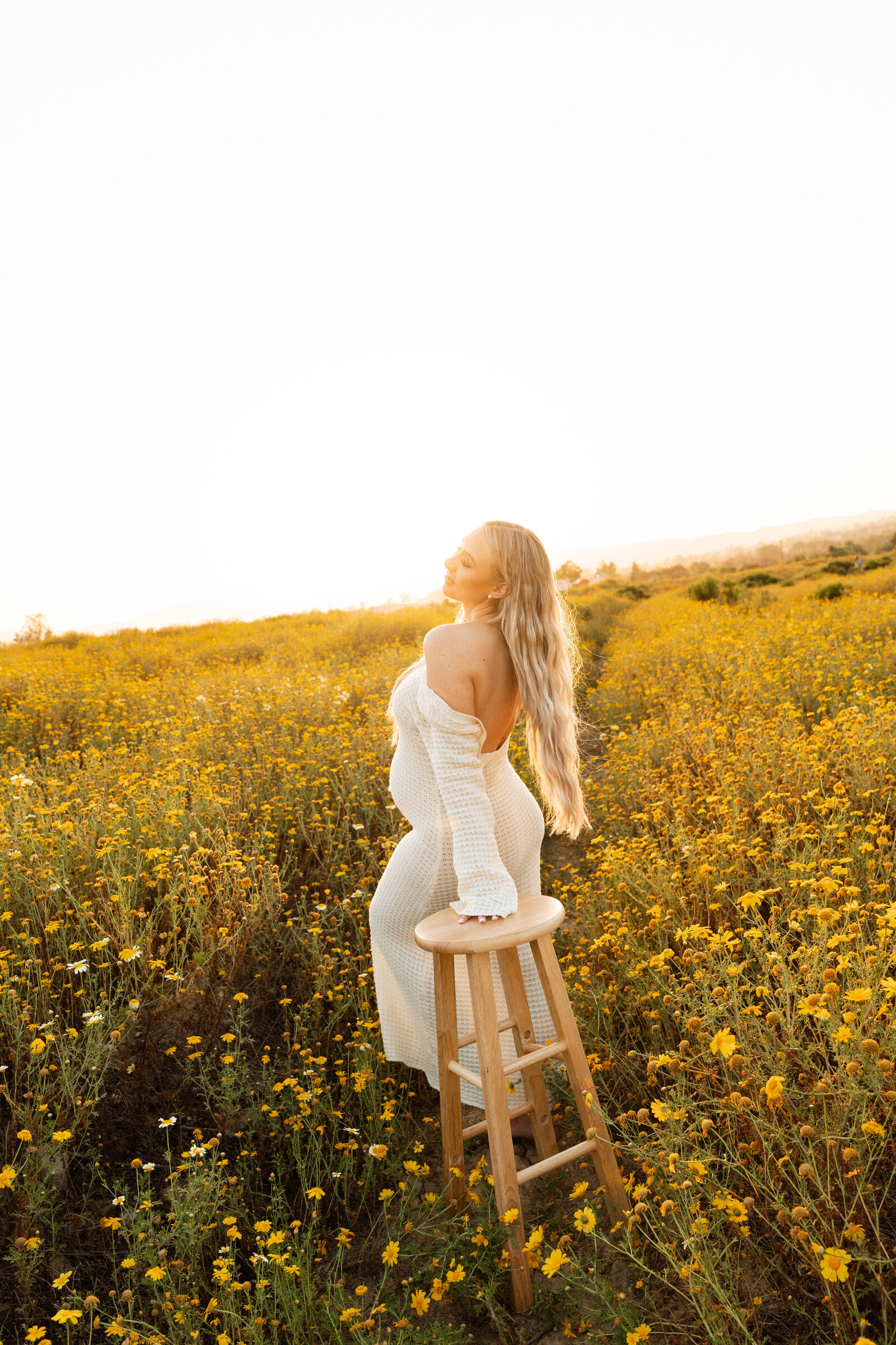 a pregnant woman leaning on a barstool in field of flowers