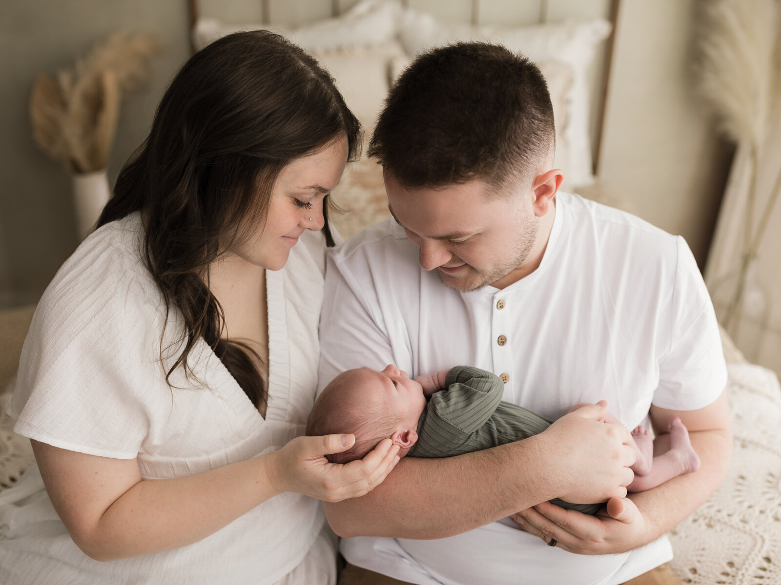 parents in white clothing holding newborn baby boy in green onesie for newborn studio portraits cleveland newborn photographer