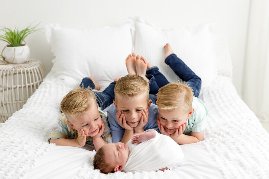 Three brothers look at their new baby brother on a bed.