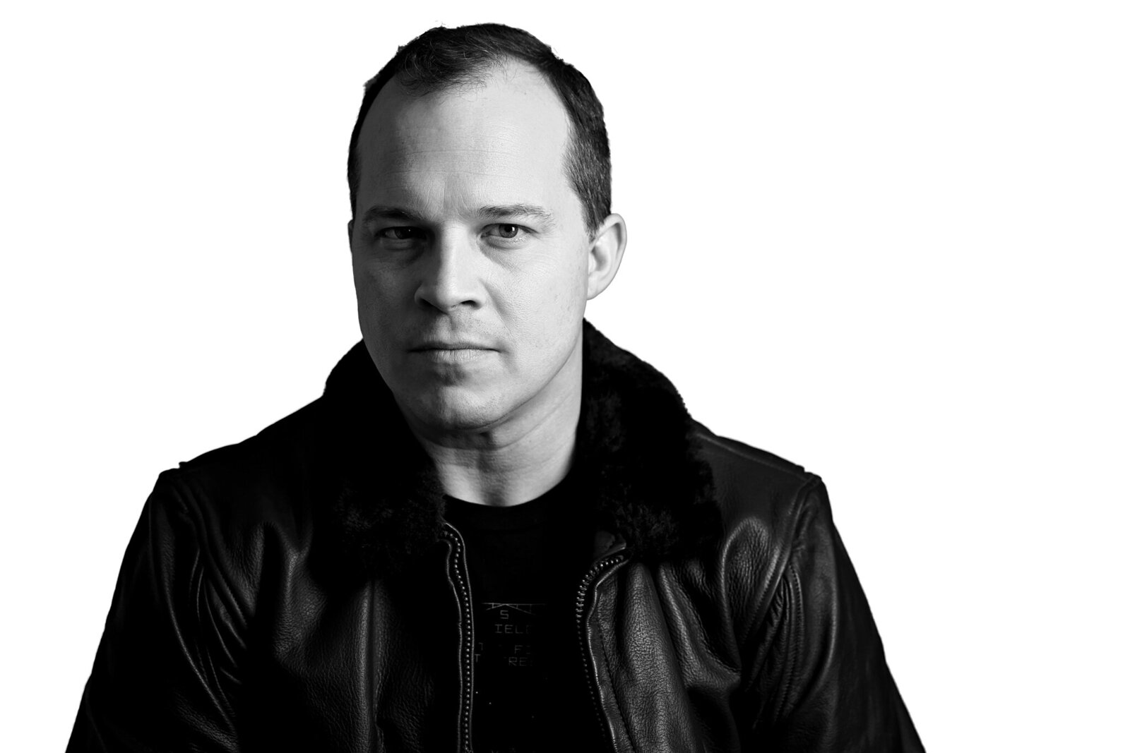 A man with short hair wearing a dark leather jacket and a black shirt, looking directly at the camera with a neutral expression, against a plain white background. Perfect for band photography Jacksonville or promo shots by a Jacksonville band photographer. The image is black and white.