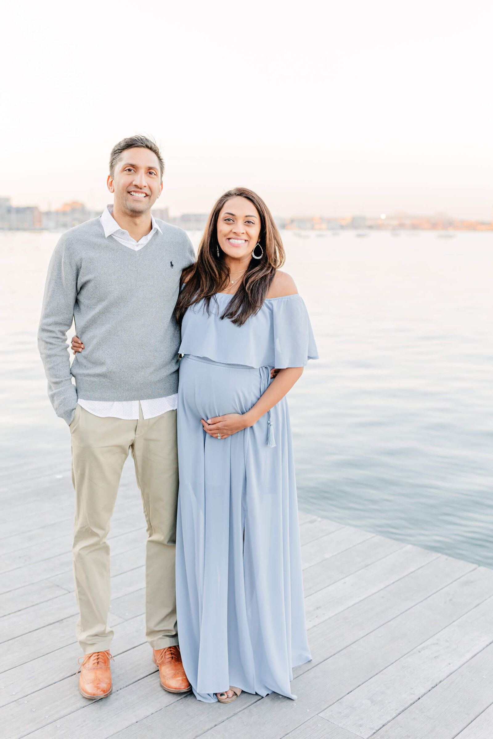 Pregnant woman and her husband smile in front of Boston Harbor