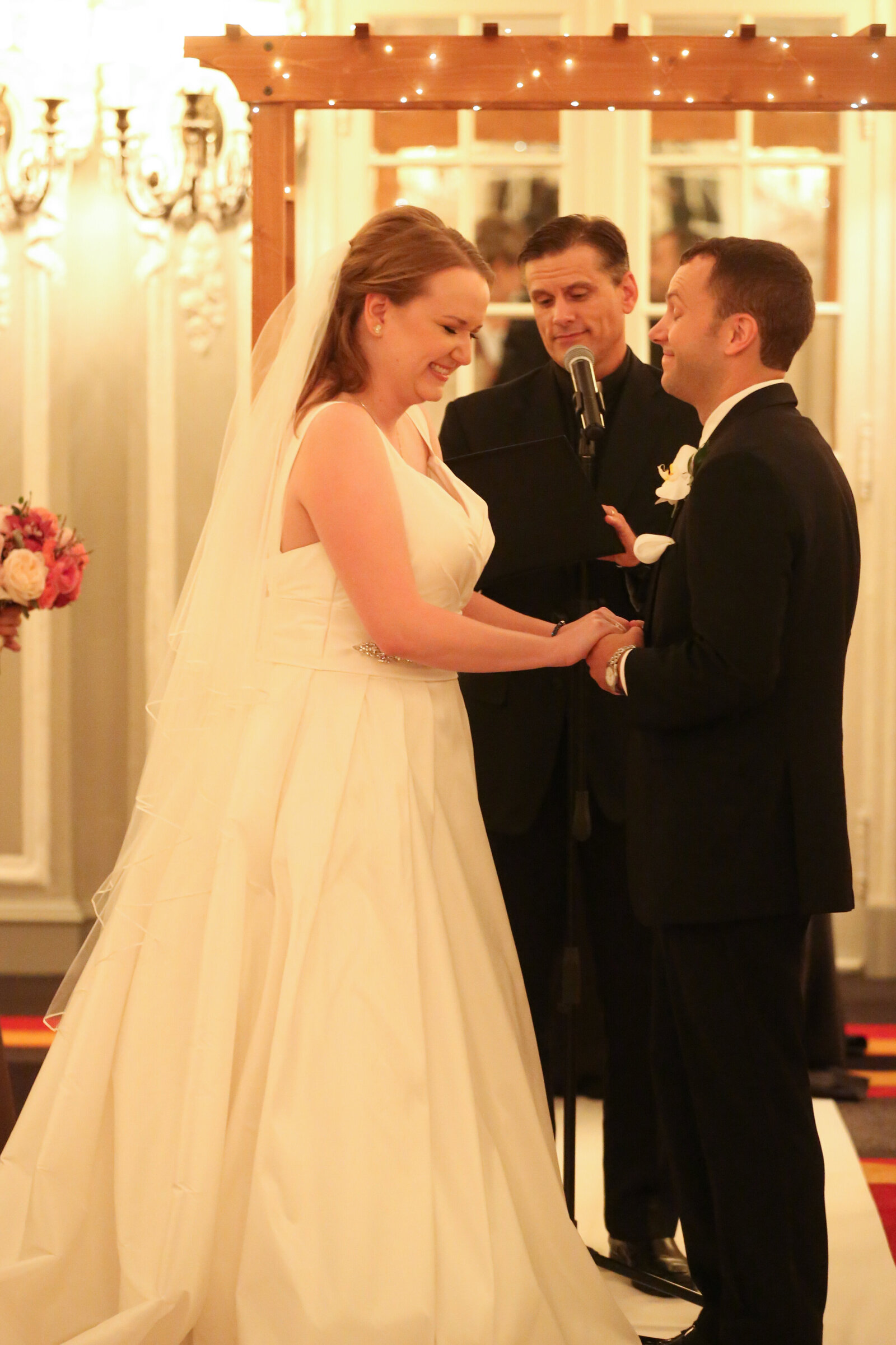 Bride laughs as she holds her groom's hands during wedding ceremony