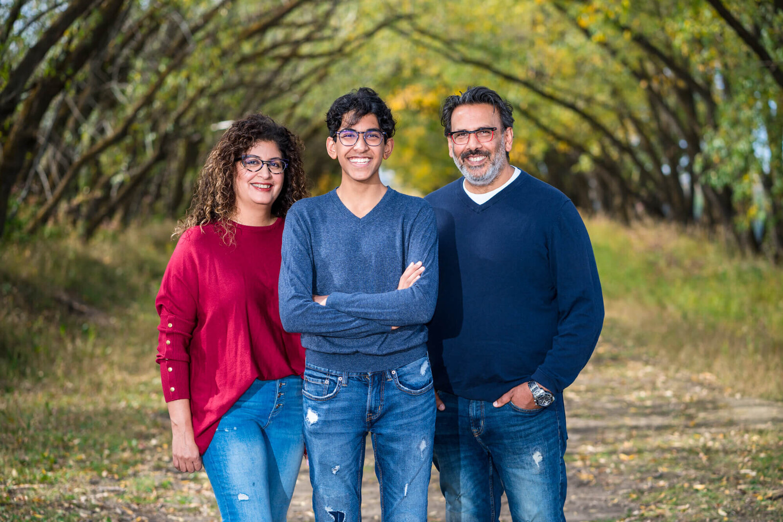 Family of 3 posed in front of arched trees