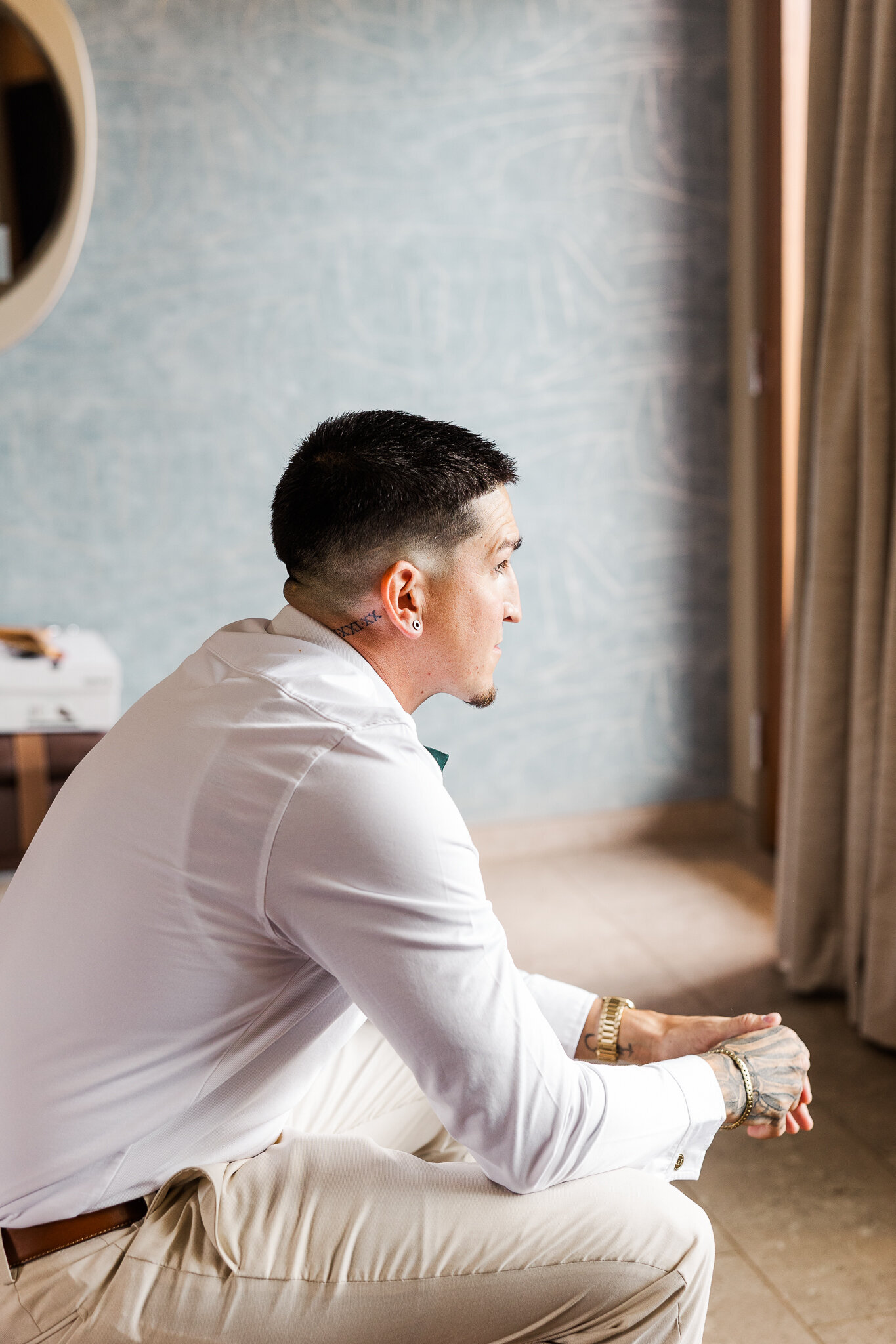 Groom sits and looks out window preparing for his Red Earth Venue Wedding