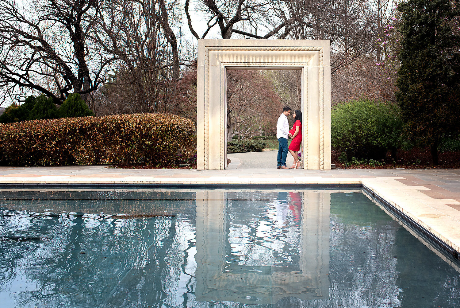 Expecting parents at a maternity photo shoot under an arch at the Dallas Arboretum.