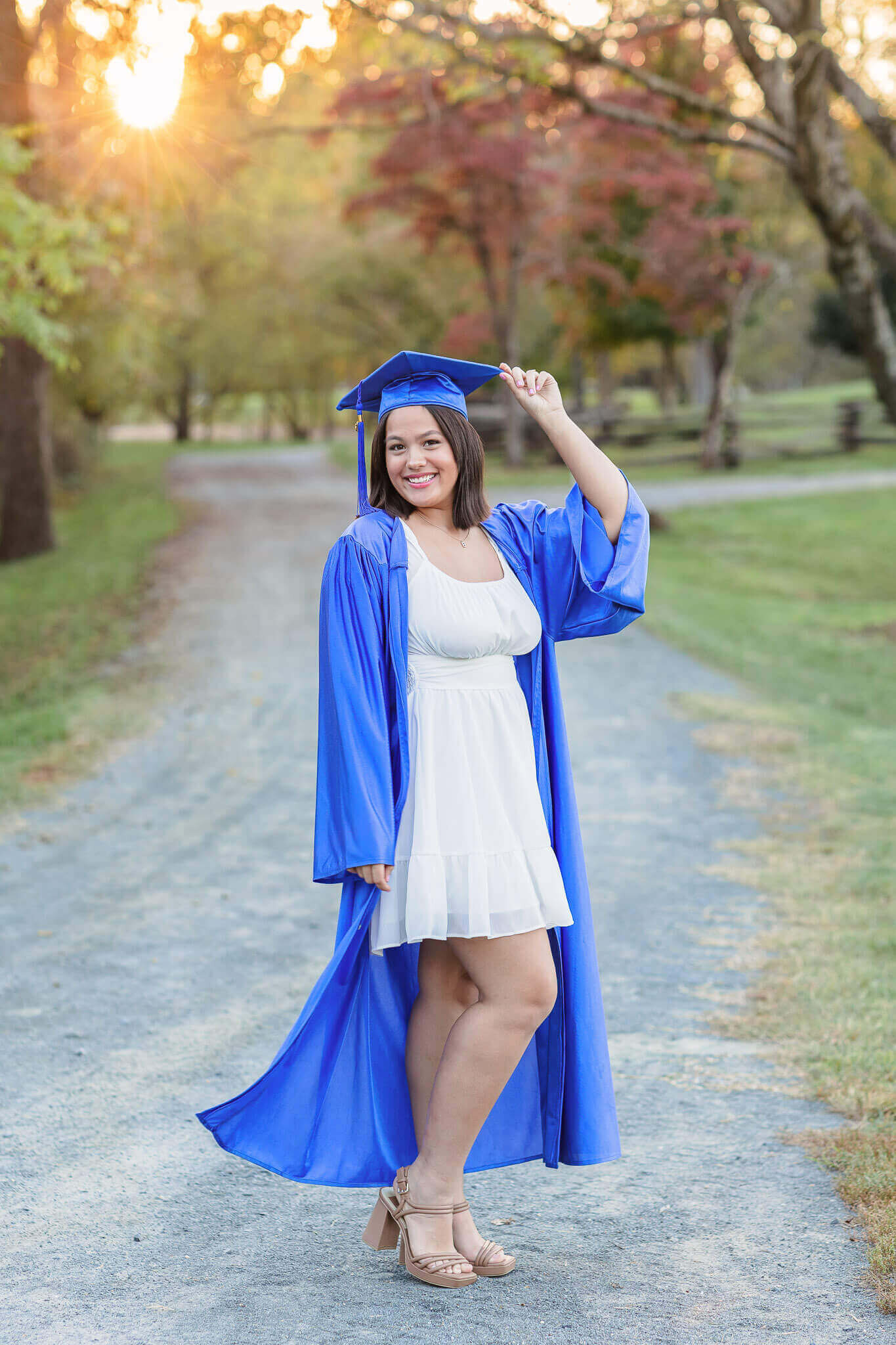 A young lady in her cap and gown at a park at sunset.