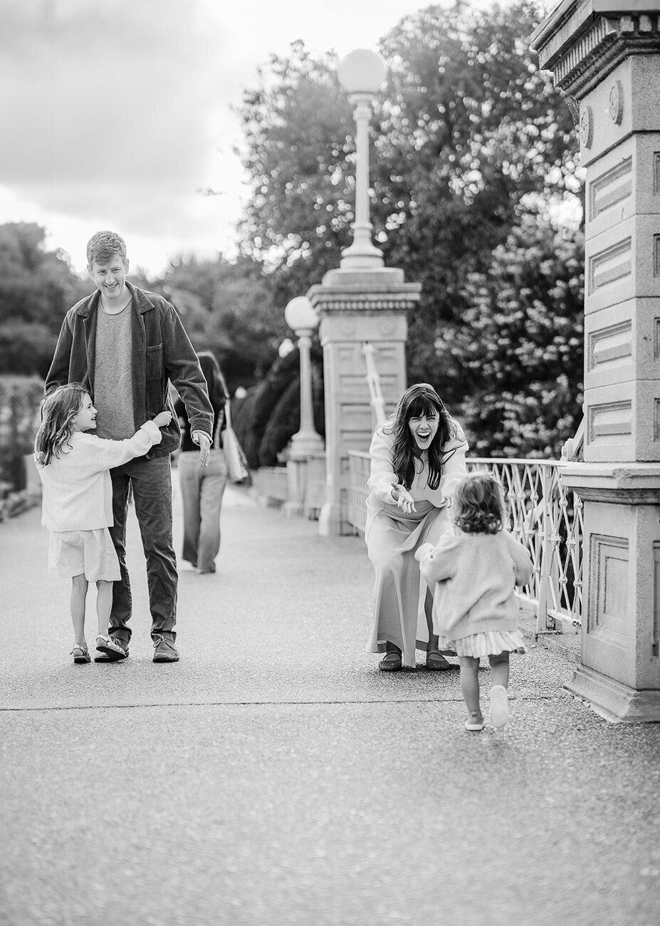 black and white image of two girls running to parents on bridge in boston public garden