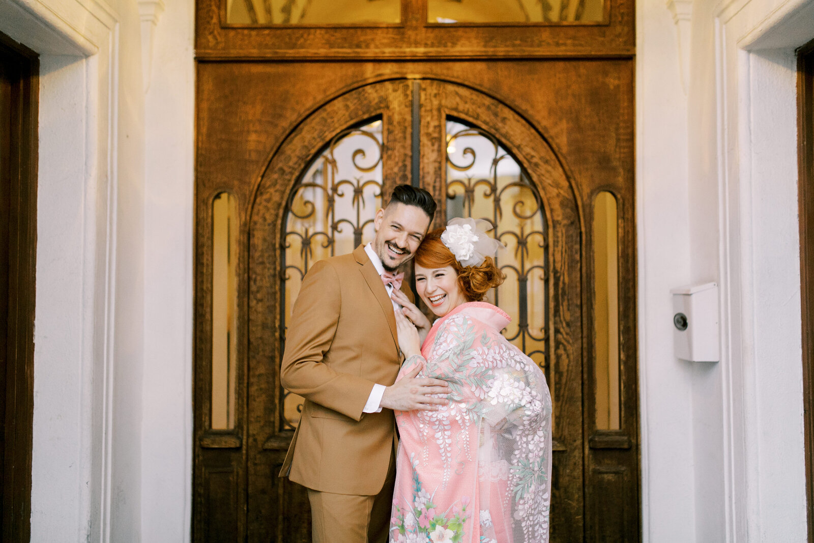 Bride in pastel pink wedding kimono with groom at ornate doorway of Carondelet House. Wedding kimono rental in Los Angeles | ロサンゼルス カロンデレットハウスで着物レンタル、装飾ドア前に立つ着物花嫁と新郎
