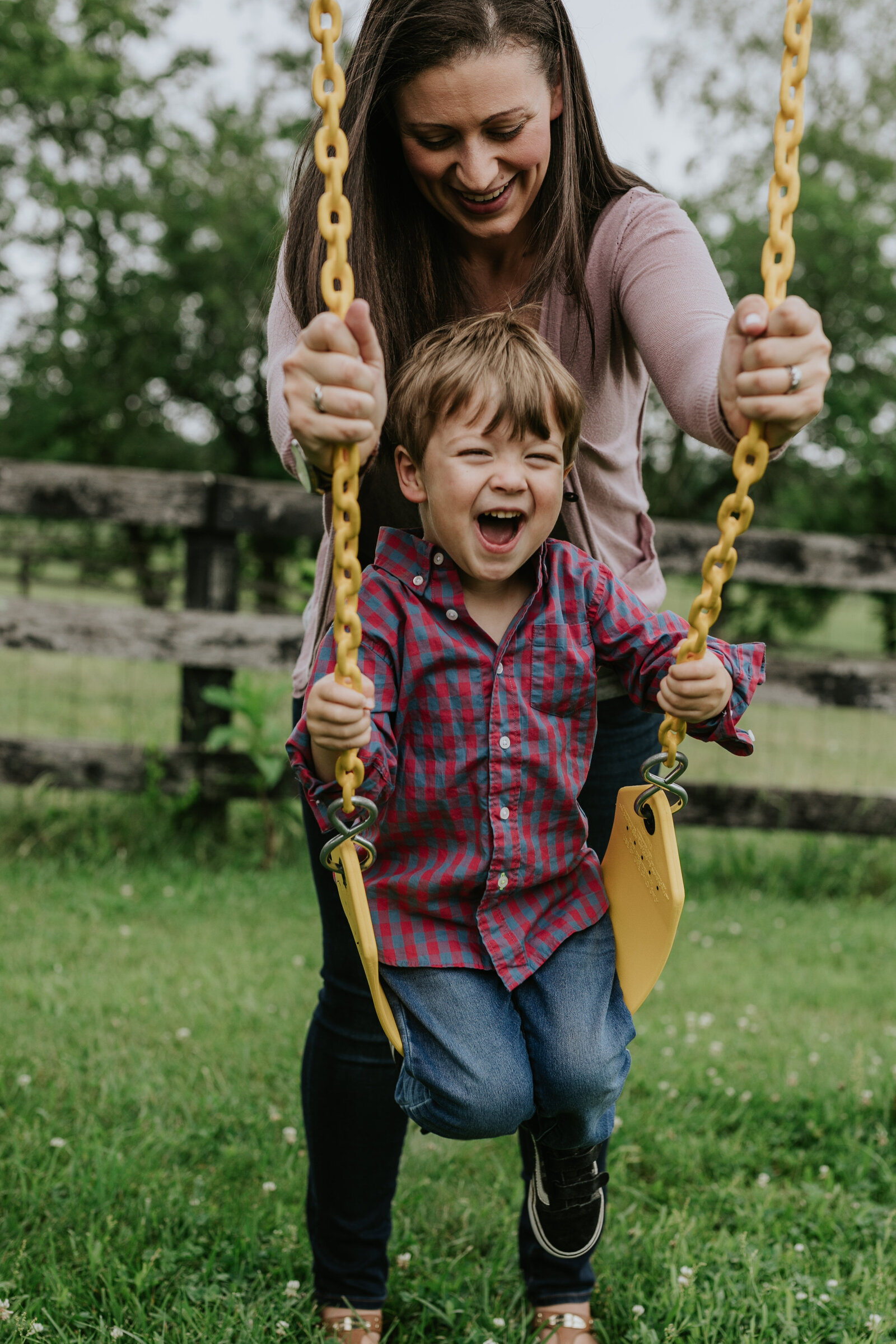 A young boy laughs as his mother pushes him on a swing