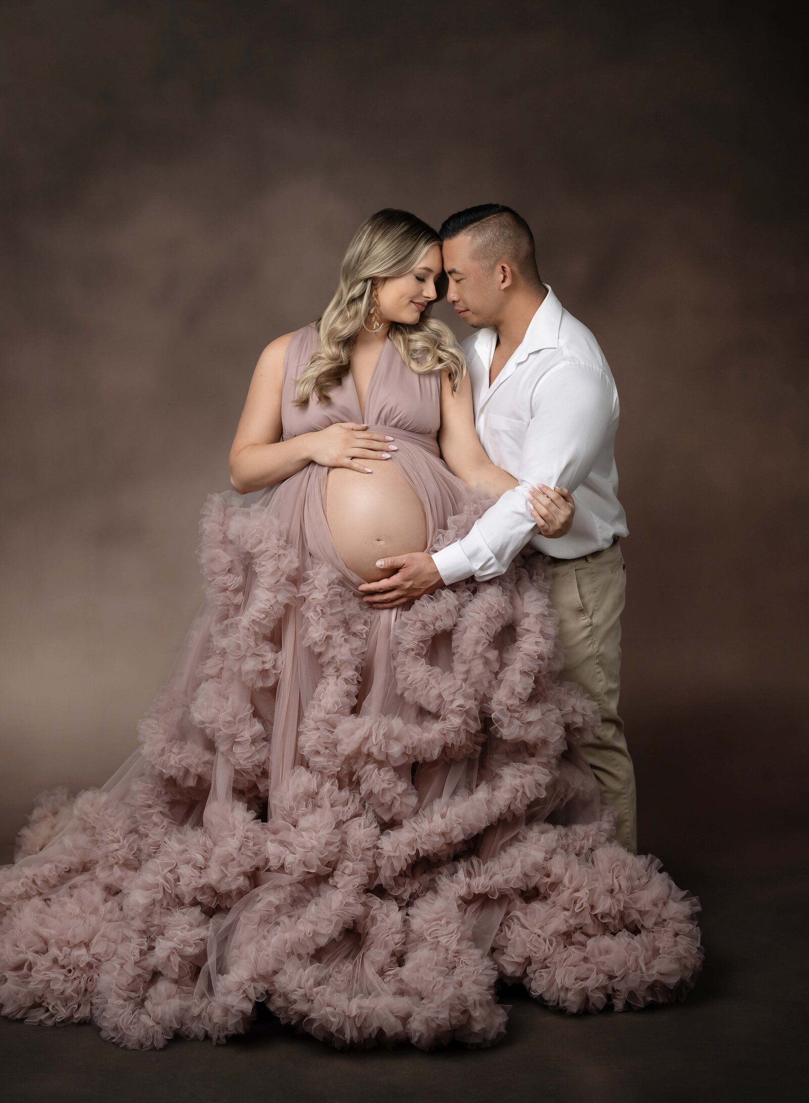 Mom and Dad cuddling for a maternity photo. mom is wearing a ruffled pink maternity gown. Maternity portrait taken by Jenni. Nikki Photography at Atlanta Photo Studio. 