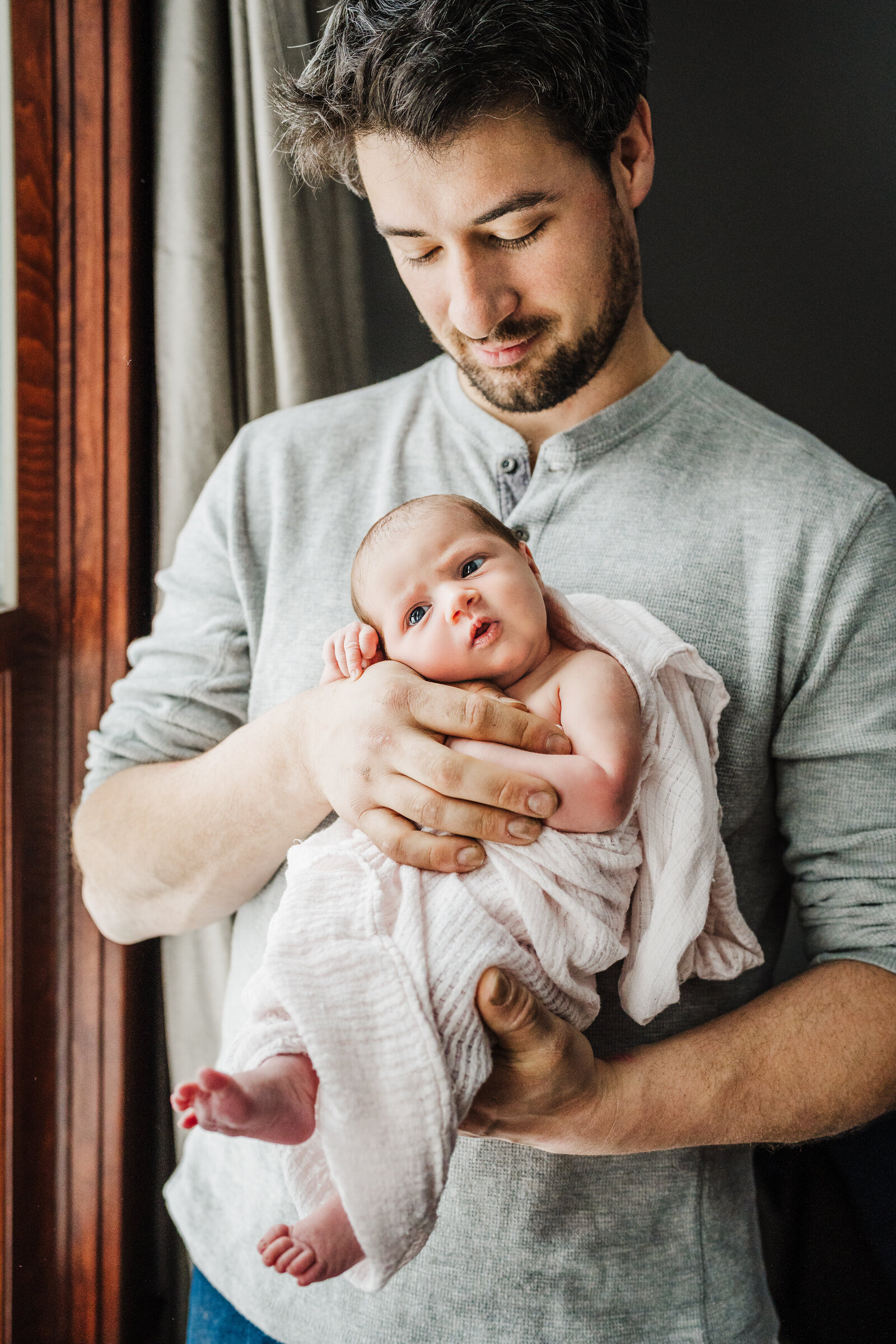 dad looks at baby girl by window