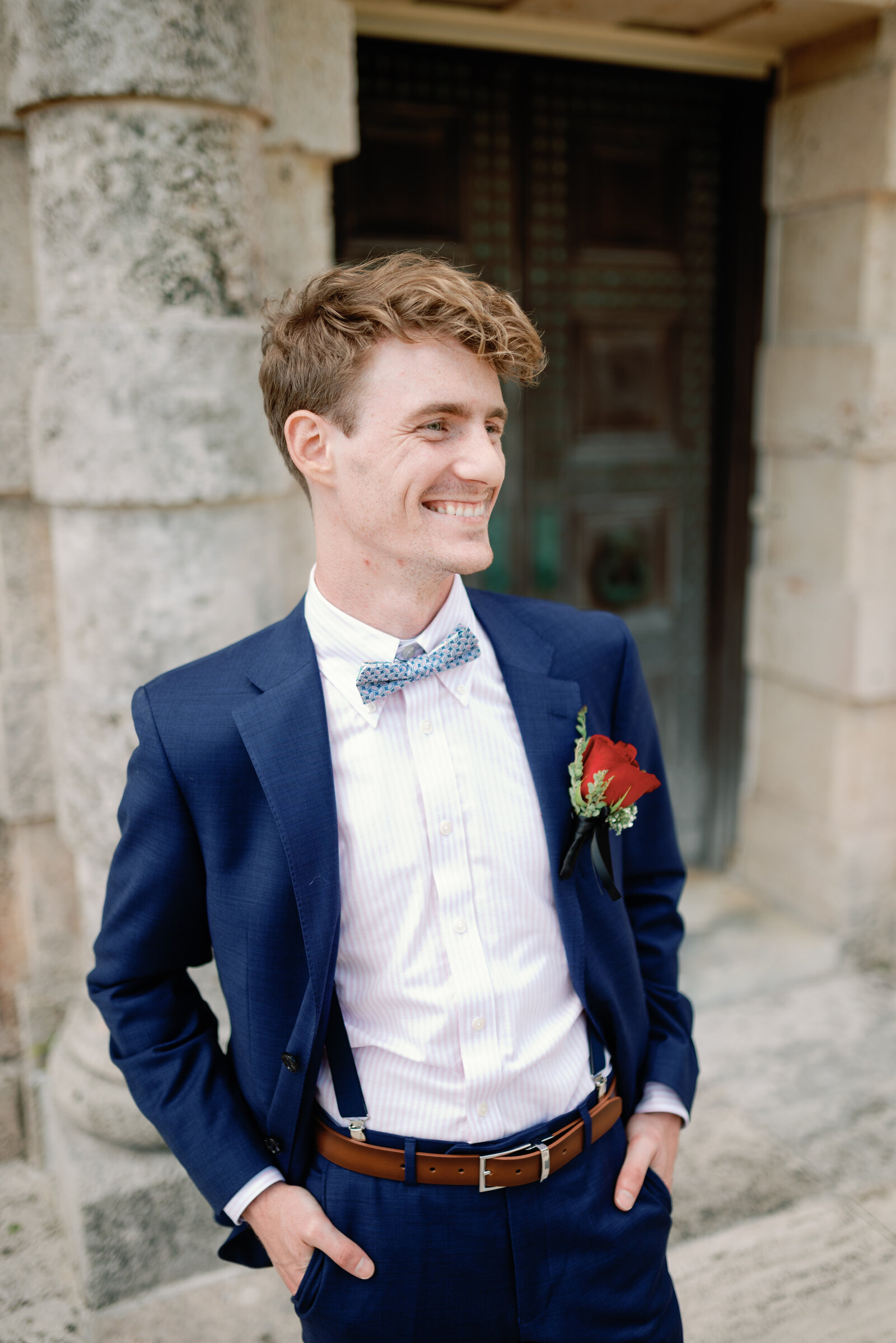 Groom standing alone, smiling with his hand in his pockets