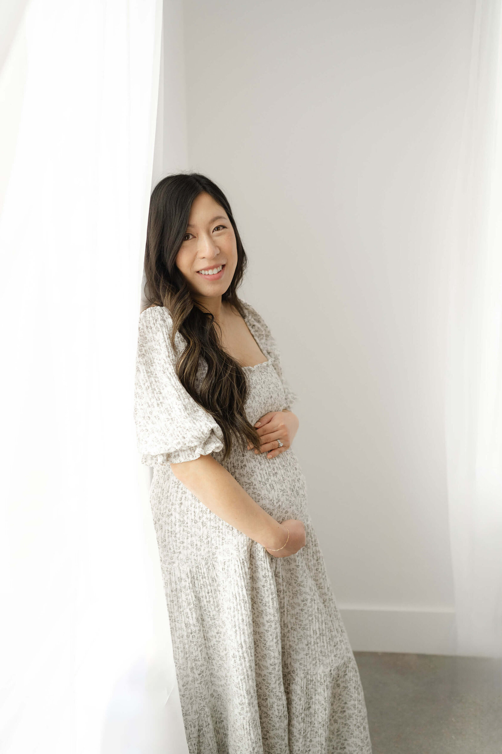 mom to be leaning on a wall as she smiles holding her baby bump