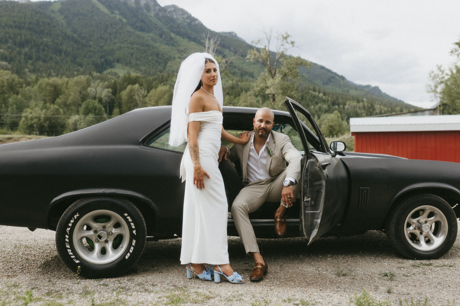 Photographer captures wedding couple in front of an old car at Alberta wedding