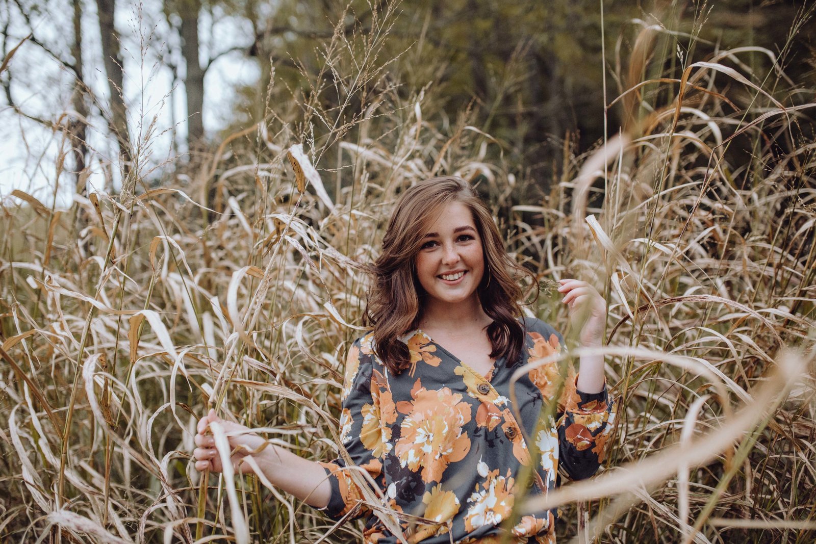 Girl in the middle of tall grass, smiling and looking at the camera.