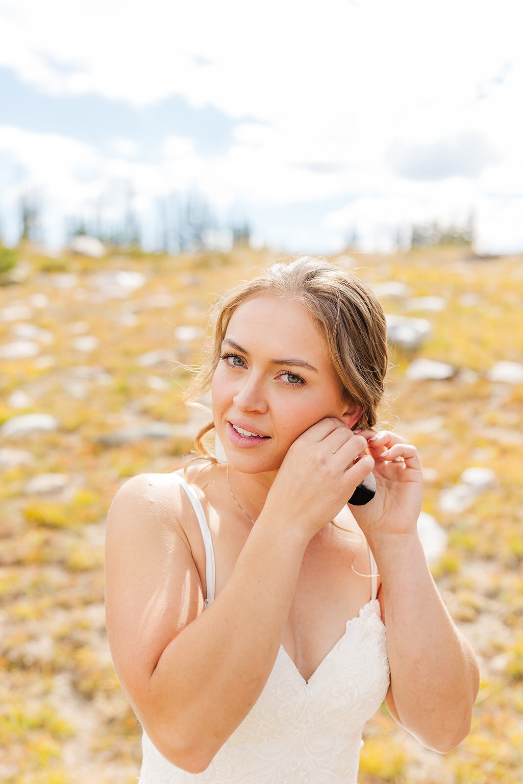 Bride posing on her wedding day putting in her earrings.