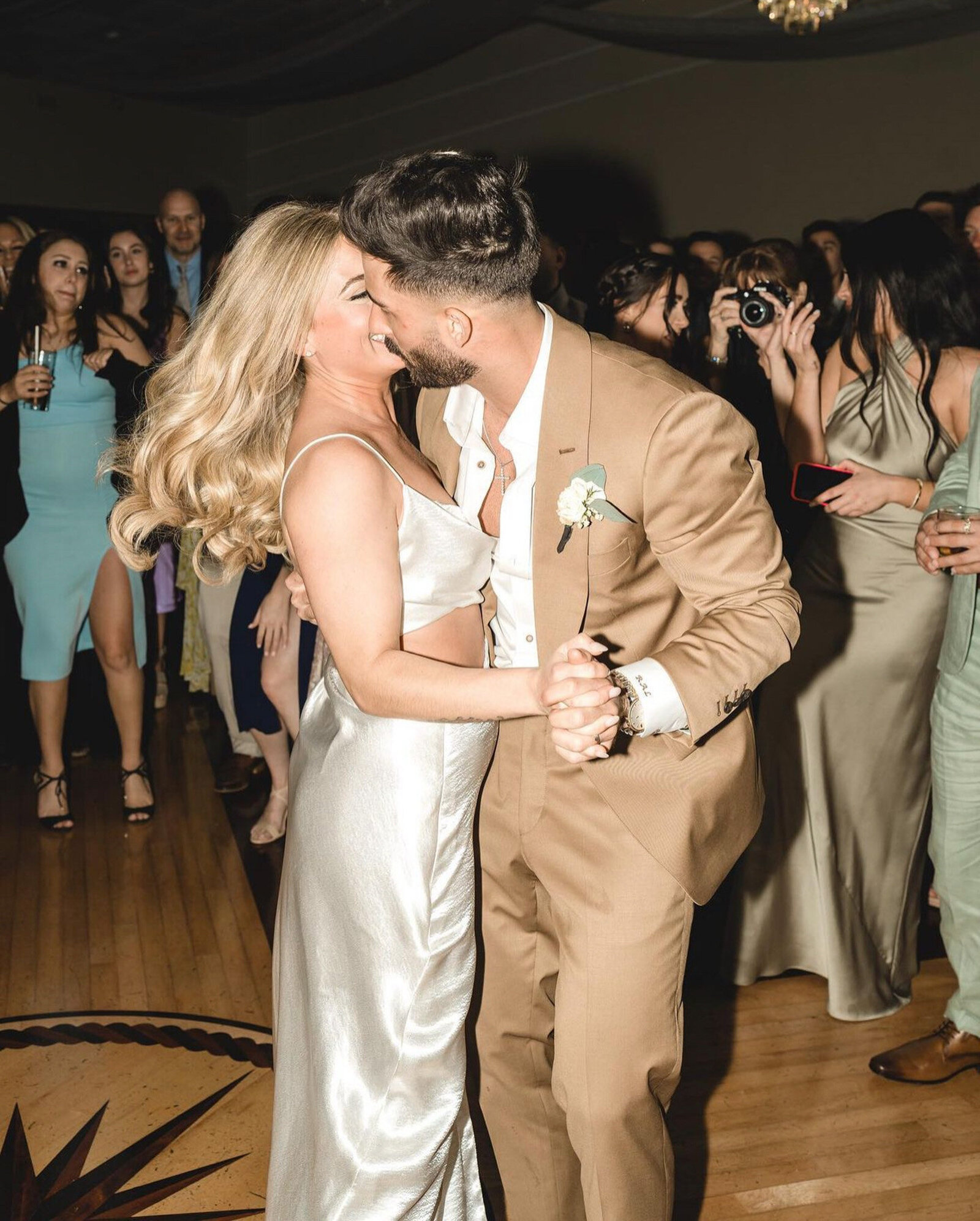 bride and groom kissing on their wedding party with the guests gather around them