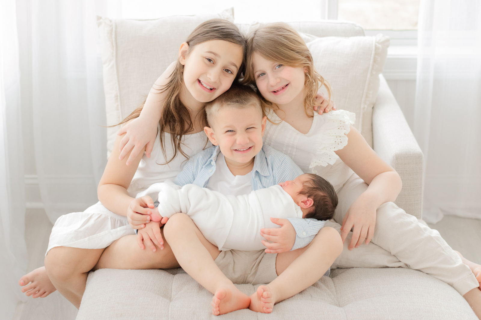 three siblings hold newborn baby brother and smile during boston newborn photos