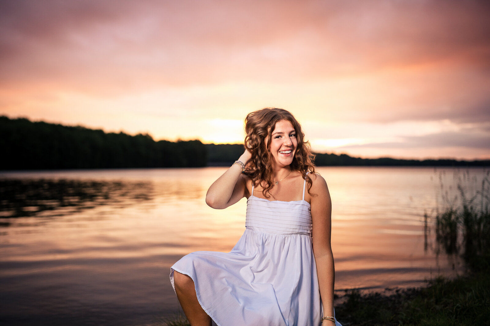 The bright orange of pink sky and the bright yellow and orange lake glisten behind this senior girls portrait