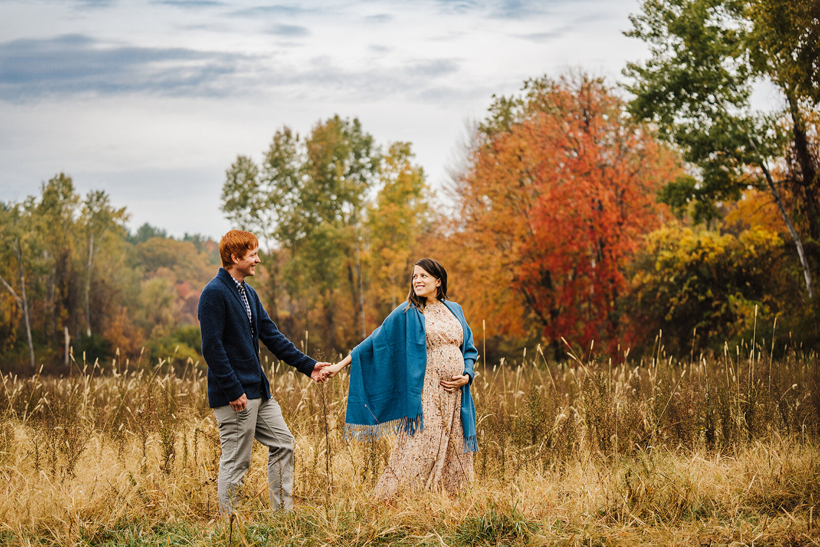 pregnant couple walks through autumn field holding hands
